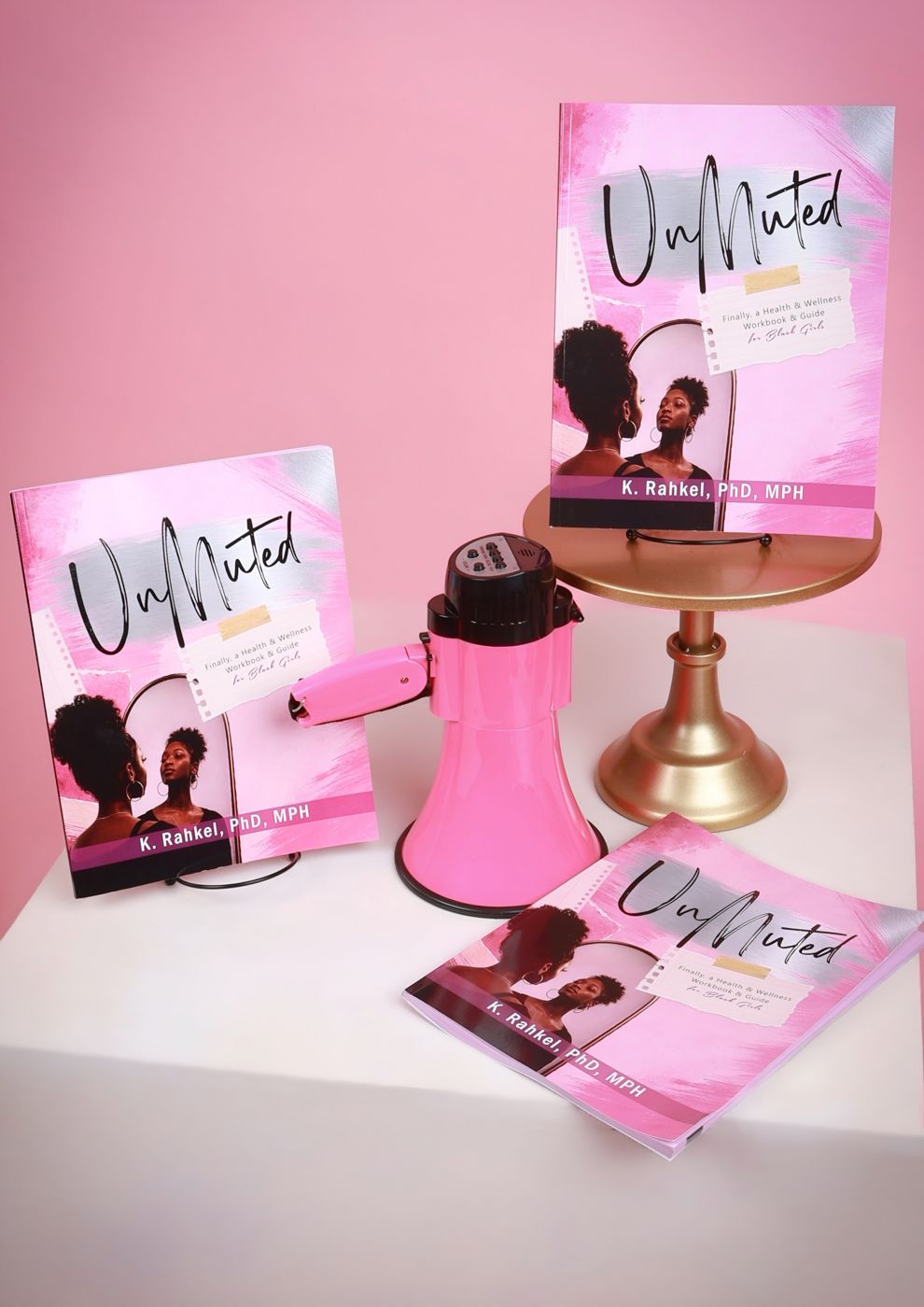 Three copies of UnMuted displayed with a pink megaphone on a gold cake stand