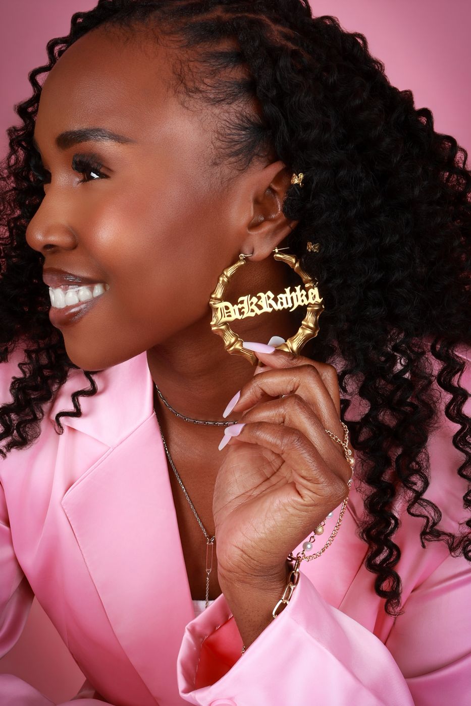 Close portrait of Dr. K. Rahkel holding a gold bamboo hoop earring that reads Dr K Rahkel